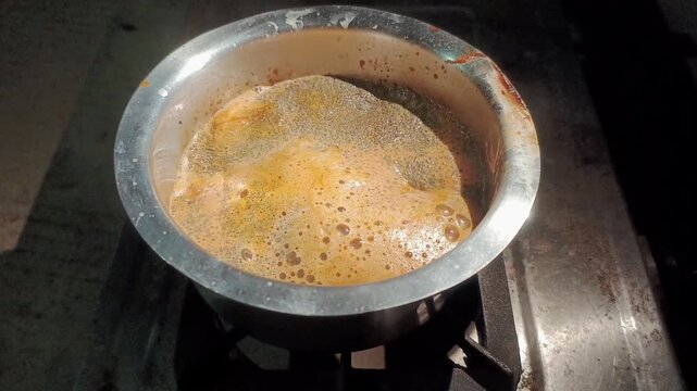 Boiling Indian masala chai tea in stainless steel vessel stirring with ladle close up