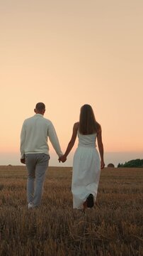 Romantic couple walking hand in hand through a tranquil harvested field at sunset, sharing an intimate peaceful moment beneath a warm pastel evening sky