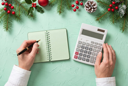 Christmas budget planning with calculator and notebook surrounded by festive evergreen decorations.