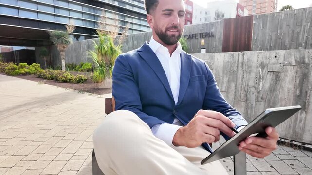 Professional businessman in smart casual clothing sitting outdoors and using a digital tablet, representing mobile work, technology and modern business lifestyle.