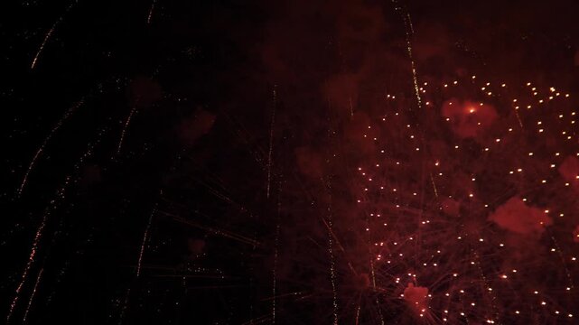 Only faint firework remnants remain against deep darkness, with tiny embers, scattered spark points, and barely visible red orange traces. Upward view feels still, minimal, and moody
