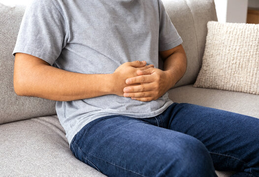 Person sitting on couch holding stomach in discomfort position