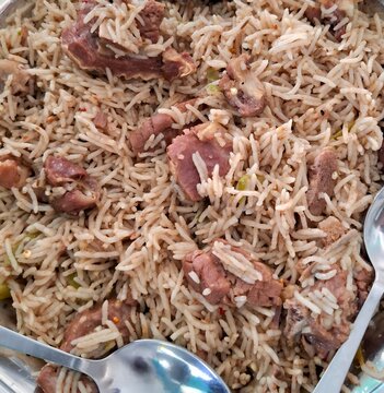 Close up of traditional mutton biryani served on a metal plate with spoons