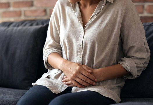 Woman sitting holding stomach in casual light colored shirt