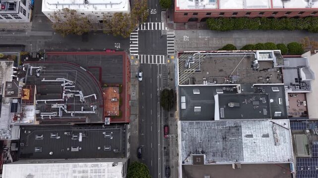 Aerial top-down view flying along a street in a downtown urban environment with cars driving and buildings on either side, showing the city grid and building rooftops in San Francisco