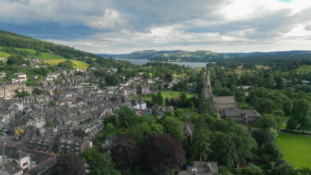 Aerial view of a historic town by a lake. Gray stone buildings line winding streets. Ambleside town sits at the head of Windermere, in the lake district Cumbria UK