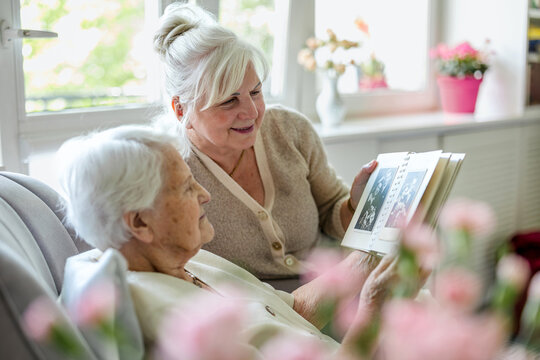 Senior woman with her caregiver looking at a photo album at home
