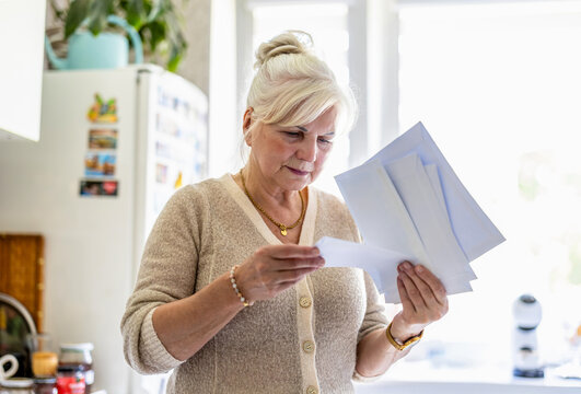 Senior woman reading her mail and documents in the kitchen
