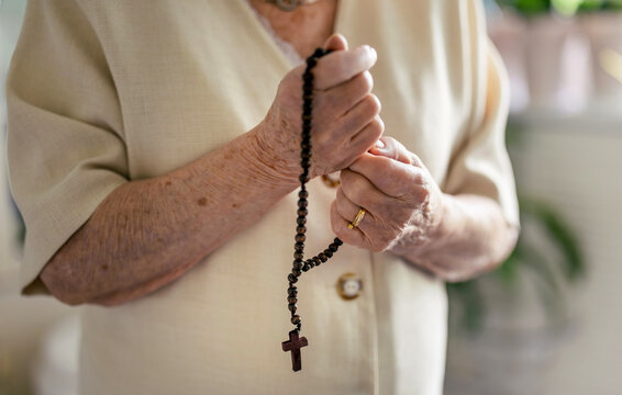 Elderly woman praying with rosary beads in her hands
