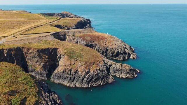 High angle aerial view of rugged coastal cliffs along Pembrokeshire coast in Wales, clear turquoise sea water washing against rocky headland, sunny summer day
