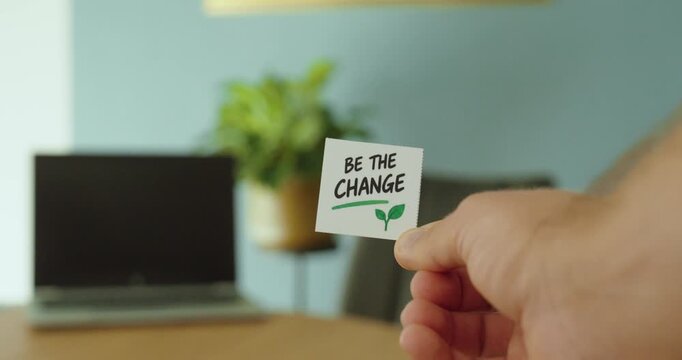 Close-up of hand holding a Be The Change message card, representing positive action, personal responsibility, growth and making a difference.