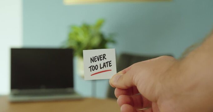 Close-up of hand holding a Never Too Late message card, representing motivation, second chances and new beginnings.
