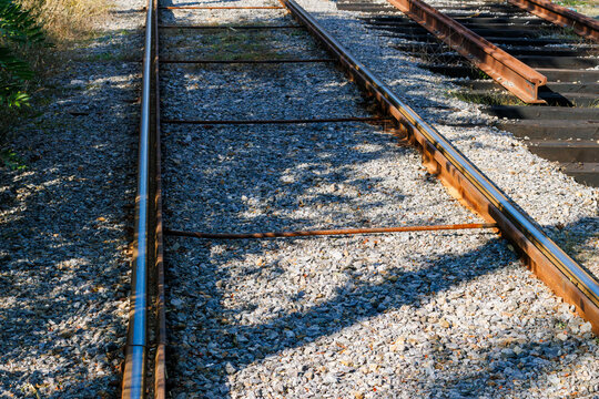 Close-up view of railway tracks running through gray gravel ballast with polished steel rail surfaces and rusted sides.