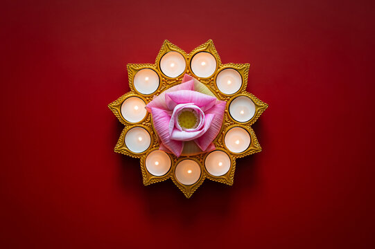 Diwali festival flat lay with a lotus flower and glowing candles on a red background.
