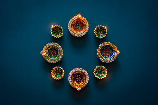 Diwali festival flat lay arrangement of glowing colorful diya lamps on dark teal background.