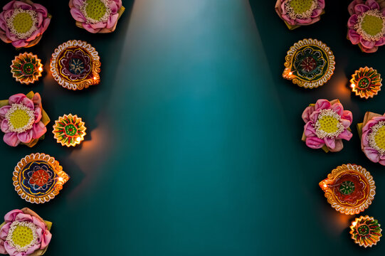 Diwali flat lay with glowing diya lamps and lotus flowers framing a teal copy space.