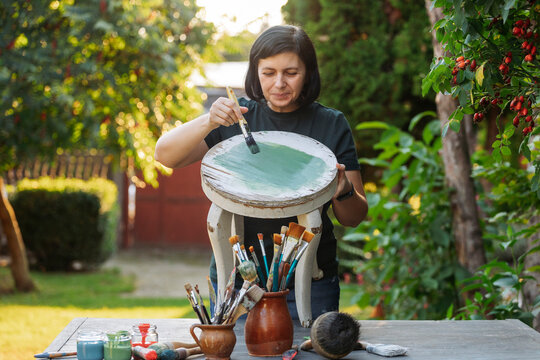 Mid woman painting furniture outdoors at home, relocation and diy concept.