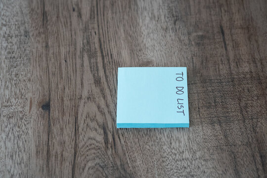 Blue sticky note pad with to do list text on dark wooden desk with copy space