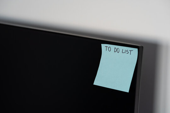 Blue sticky note with to do list text stuck on computer monitor corner