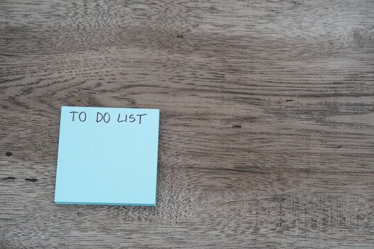 Blue sticky note pad with to do list text on dark wooden desk with copy space