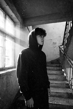 Melancholischer junger Mann im Hoodie im Treppenhaus &ndash; K&uuml;nstlerisches Schwarzwei&szlig;-Portr&auml;t mit dramatischem Lichtstrahl   