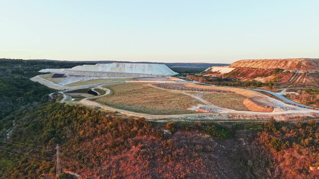 The scene shows a large quarry with white stone piles at sunset in Texas. The area has dirt roads and some vegetation on the hills nearby.