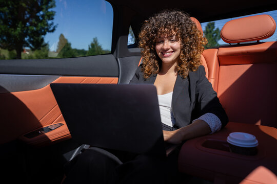 Businesswoman working on laptop inside car with orange leather seats