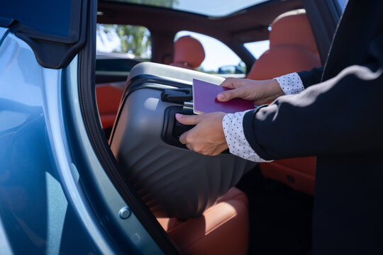 Businesswoman loading suitcase into car with passport during travel