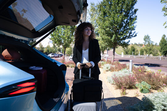 Businesswoman with luggage standing by car trunk in parking lot