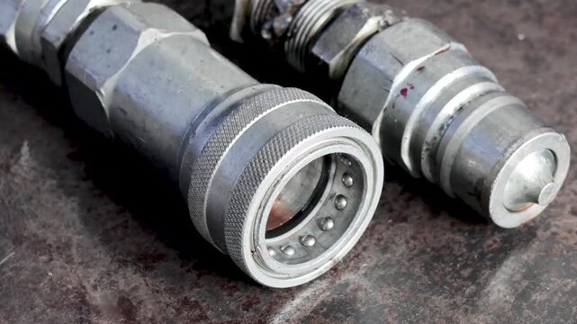 Metallic hydraulic quick disconnect couplings resting on steel workbench inside industrial workshop.