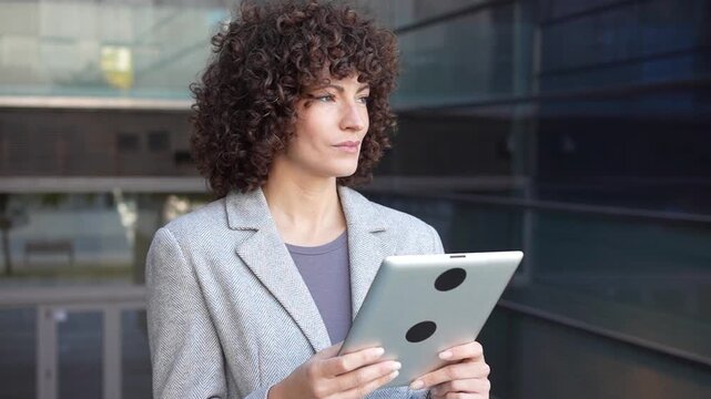 A businesswoman is engaging thoughtfully with a tablet in a vibrant modern urban environment