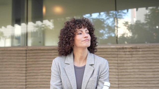 A cheerful woman with curly hair is happily holding a water bottle while outdoors in nature