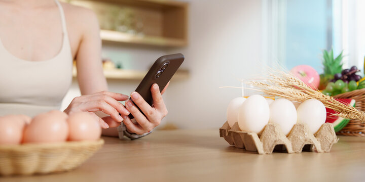 Cropped shot of woman using smartphone at table with fresh eggs and healthy food