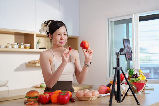 Asian woman filming nutrition vlog with smartphone on tripod in kitchen