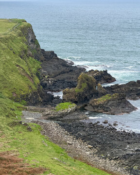 Steep green cliffs and dark volcanic rock formations meet the North Atlantic near Giant's Causeway on the rugged Causeway Coast of Northern Ireland.