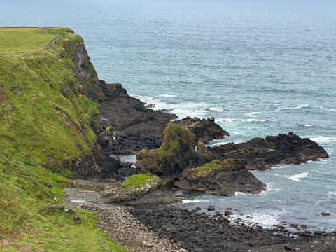 Steep green cliffs and dark volcanic rock formations meet the North Atlantic near Giant's Causeway on the rugged Causeway Coast of Northern Ireland.