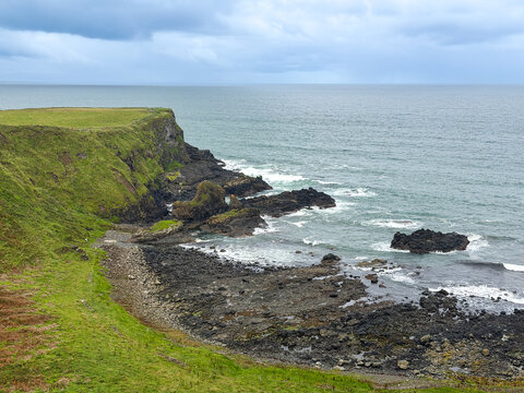 Green cliffs descend to a rugged volcanic shoreline beneath stormy clouds near Giant's Causeway on the Causeway Coast of Northern Ireland.