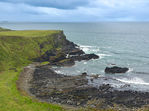 Dark volcanic rocks and grassy cliffs border the North Atlantic beneath stormy clouds along the Causeway Coast near Giant's Causeway, Northern Ireland.