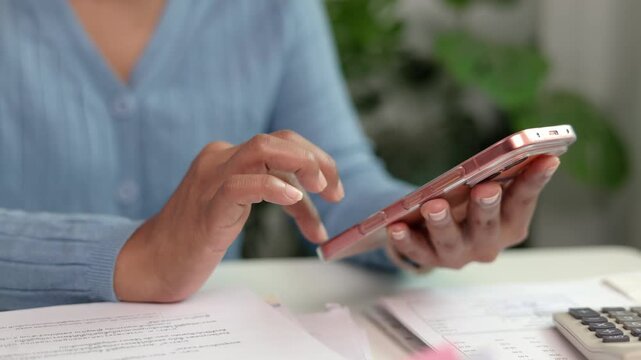 Female worker swiping screen on smart phone to reply business email sitting in contemporary workspace with paperwork and office desk organization during busy office work hours