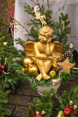 Fototapeta premium Gold Christmas Angel Decoration. Gold angel figurine surrounded by evergreen branches, Christmas ornaments, pine cones, wooden star. Christmas angel arrangement, traditional festive holiday decoration