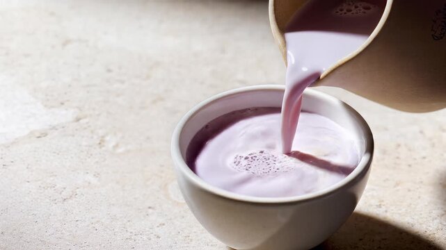 Fresh purple taro milk pouring into a white ceramic bowl