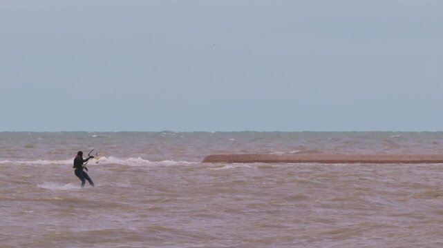 Action shot of a lone kitesurfer with kite gliding across rough ocean waters on an overcast day. Extreme water sports and active lifestyle concept. Flying over water in slow motion..
