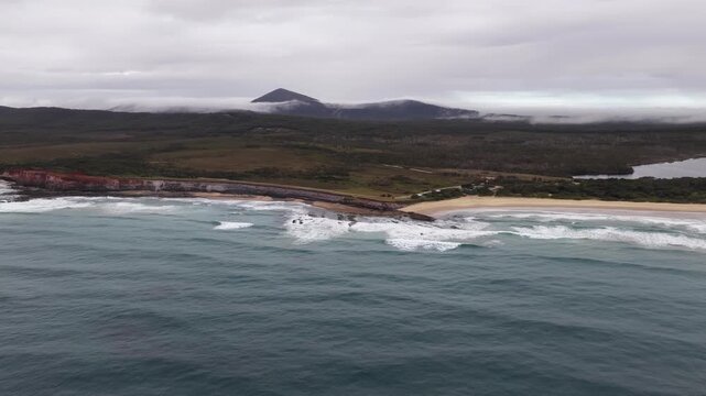 Aerial video flying over the rugged coastline at Lake Arragan, featuring sandy shoreline, rocky formations and waves rolling in from the Pacific Ocean