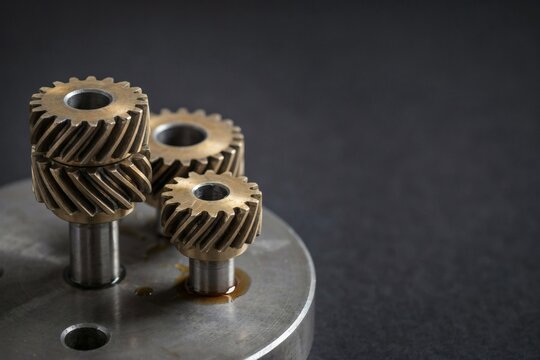 Three brass helical gears mounted on steel shafts across an oiled machine plate