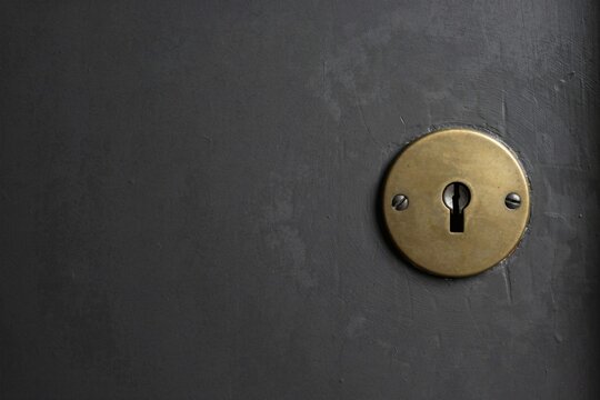 Aged brass keyhole escutcheon set into a dark grey door with generous copy space