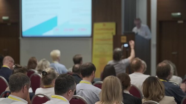 Conference attendees listen to speaker presenting slides in professional seminar room, networking and learning in formal business event.