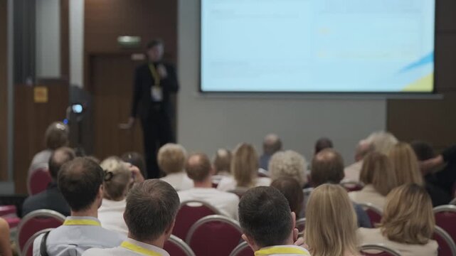 Conference audience listening to presenter during professional seminar, projector screen visible, participants seated, corporate training, networking atmosphere.