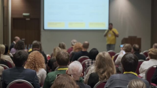 Conference audience listens to presenter during business seminar in hotel meeting room. Emphasis on engagement, learning, networking, professional event atmosphere.