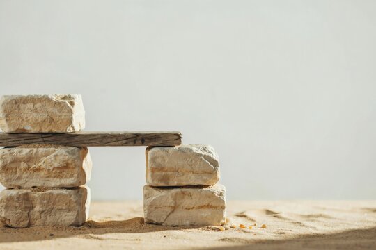 Weathered plank bridging stacked limestone blocks on sand under bright daylight