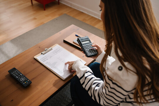 Person using calculator at home while organizing notes and planning budget on coffee table today now